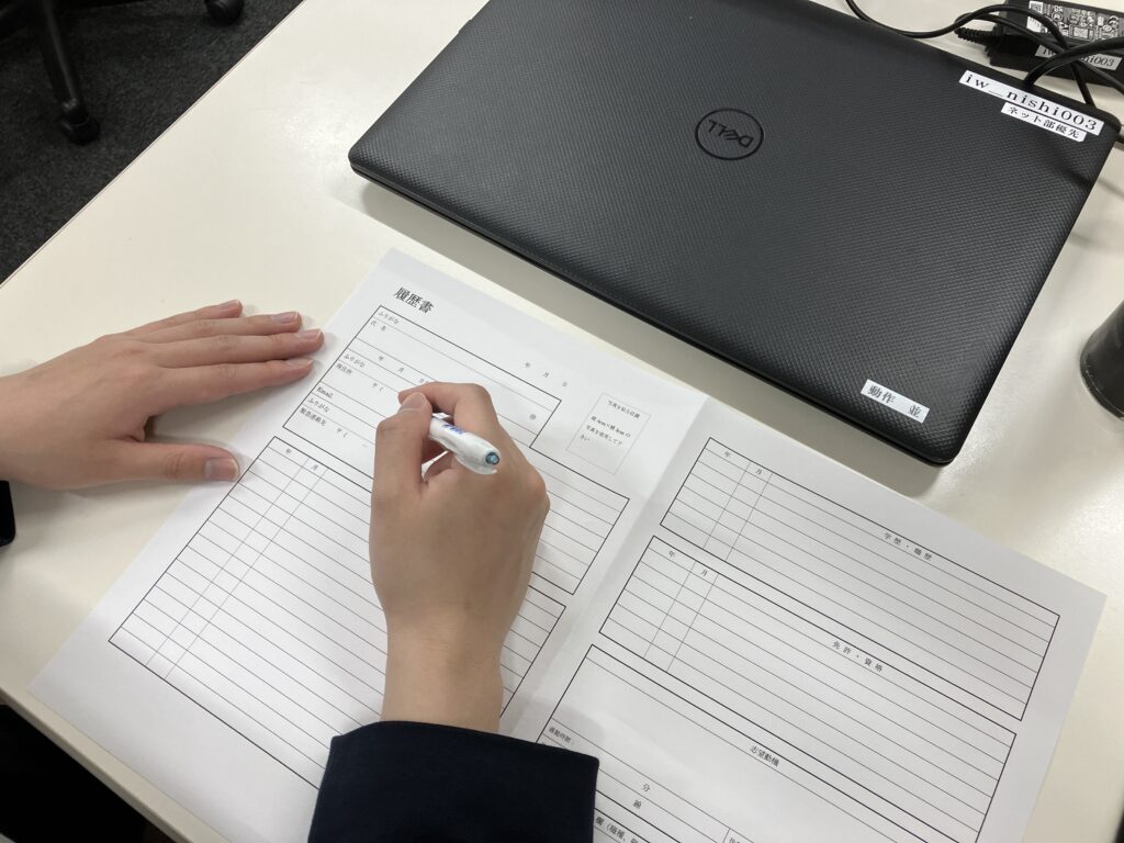 パソコンの横で、応募書類に記入している手元の様子