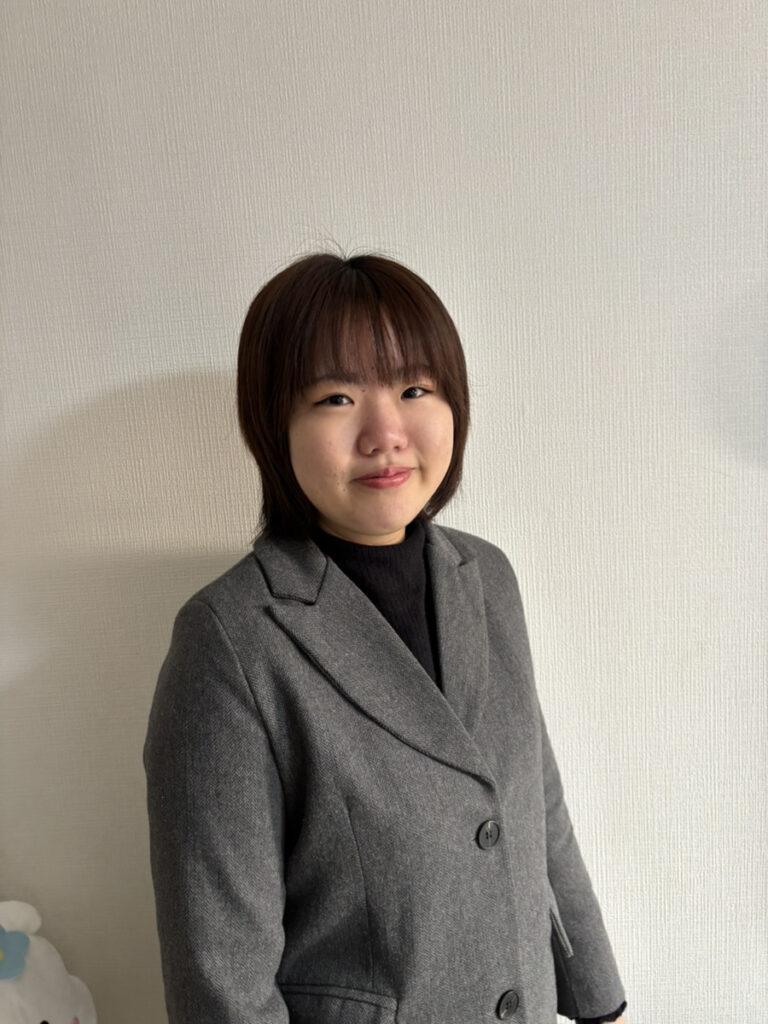 アイ・ワークススタッフ、田原の写真。茶色のボブヘアで、グレーのジャケットと黒のインナーを着用し、穏やかな表情で微笑んで正面を向いているポートレート。