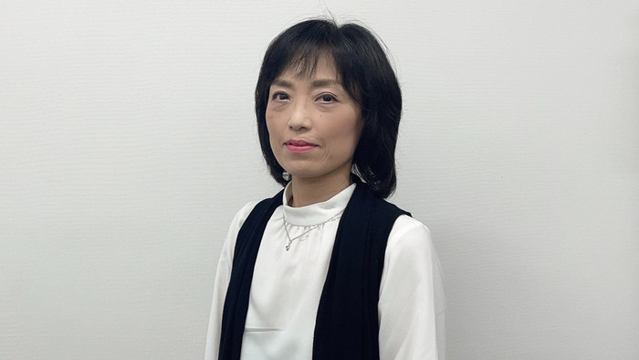 アイ・ワークススタッフ、竹島の写真。黒髪のショートヘアで、白のブラウスに黒のベストを羽織り、シルバーのネックレスを着用。穏やかな表情で正面を見つめるポートレート。